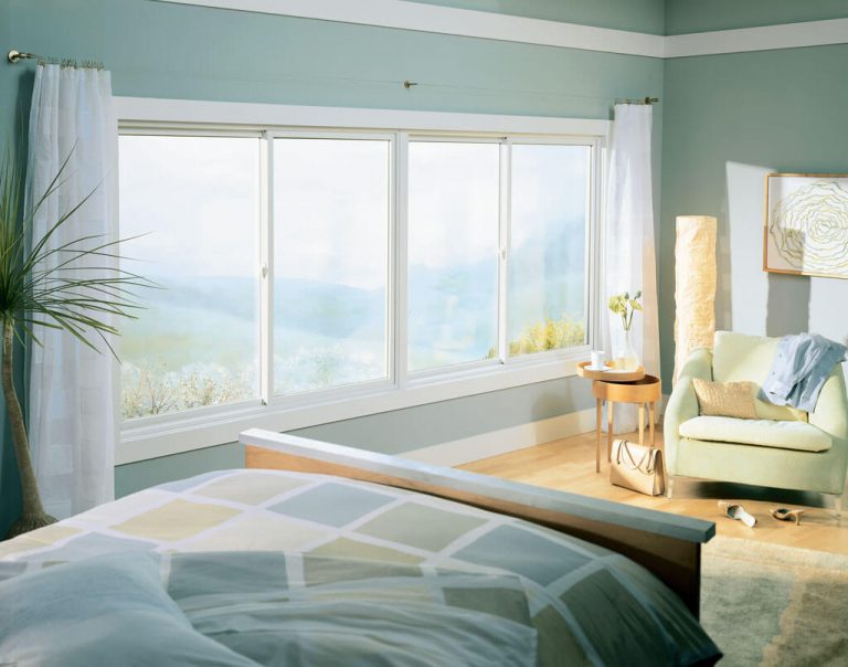 Imagem onde se vê o interior de um quarto com amplas janelas de vidro, cama de casa, poltrona